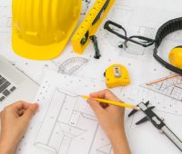 Hand over Construction plans with yellow helmet and drawing tools on blueprints